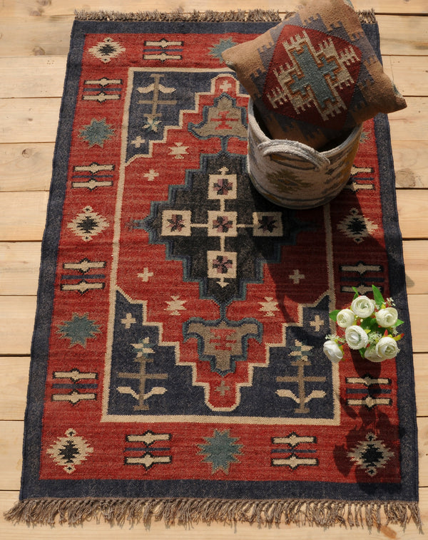 Handwoven red and navy blue tribal wool area rug with geometric Southwestern pattern and fringe, displayed on a natural wooden floor.