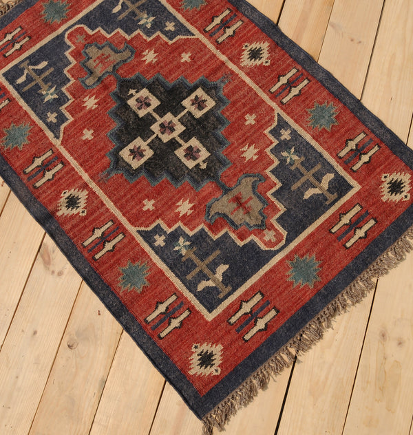Handwoven red and navy blue tribal wool area rug with geometric Southwestern pattern and fringe, displayed on a natural wooden floor.