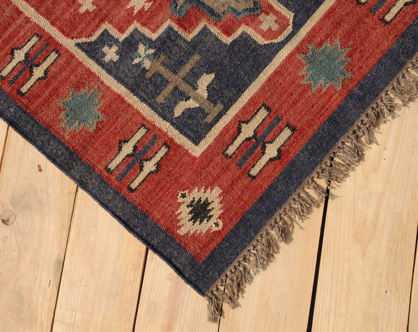 Handwoven red and navy blue tribal wool area rug with geometric Southwestern pattern and fringe, displayed on a natural wooden floor.