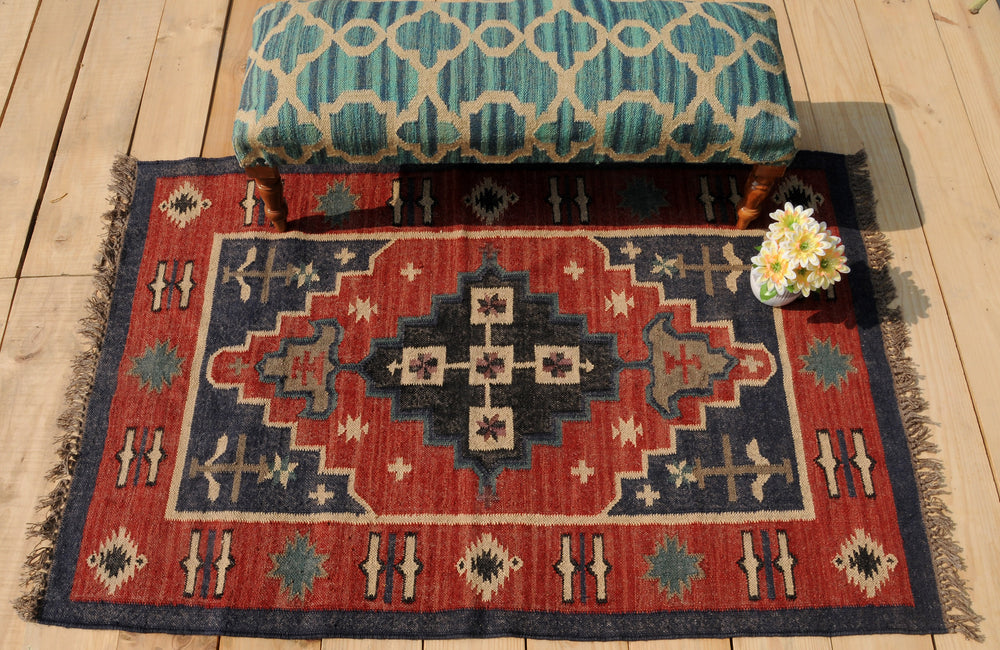 Handwoven red and navy blue tribal wool area rug with geometric Southwestern pattern and fringe, displayed on a natural wooden floor.