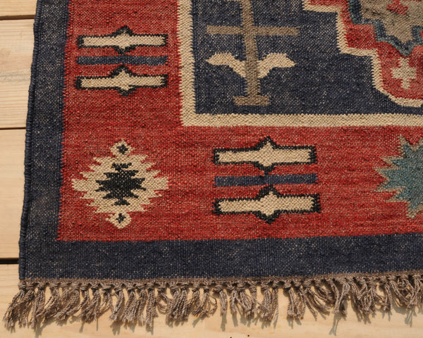 Handwoven red and navy blue tribal wool area rug with geometric Southwestern pattern and fringe, displayed on a natural wooden floor.