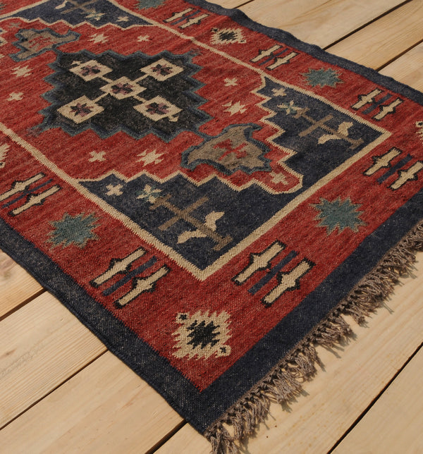 Handwoven red and navy blue tribal wool area rug with geometric Southwestern pattern and fringe, displayed on a natural wooden floor.