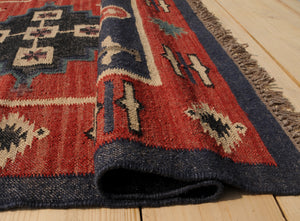 Handwoven red and navy blue tribal wool area rug with geometric Southwestern pattern and fringe, displayed on a natural wooden floor.