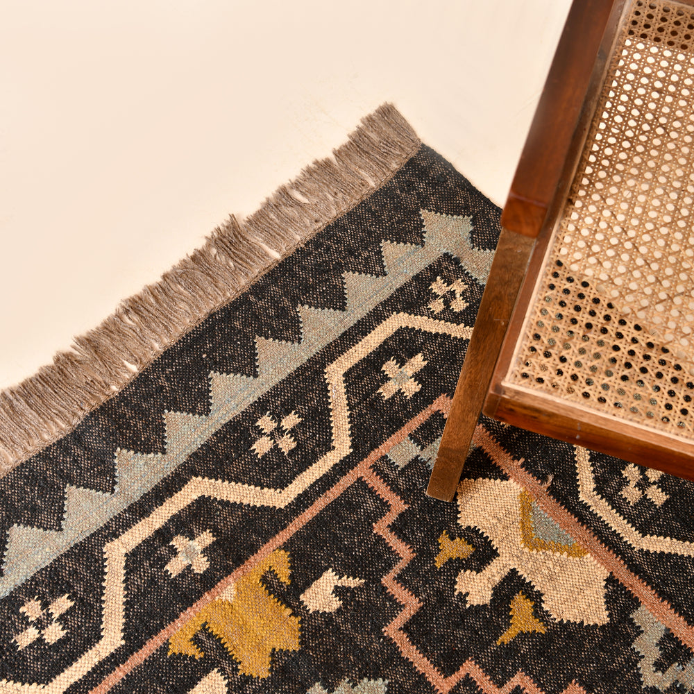 Handwoven black wool jute Kilim area rug with tribal geometric pattern and fringe in a modern living room.
