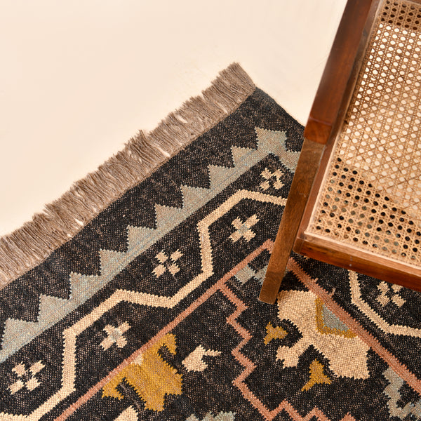 Handwoven black wool jute Kilim area rug with tribal geometric pattern and fringe in a modern living room.