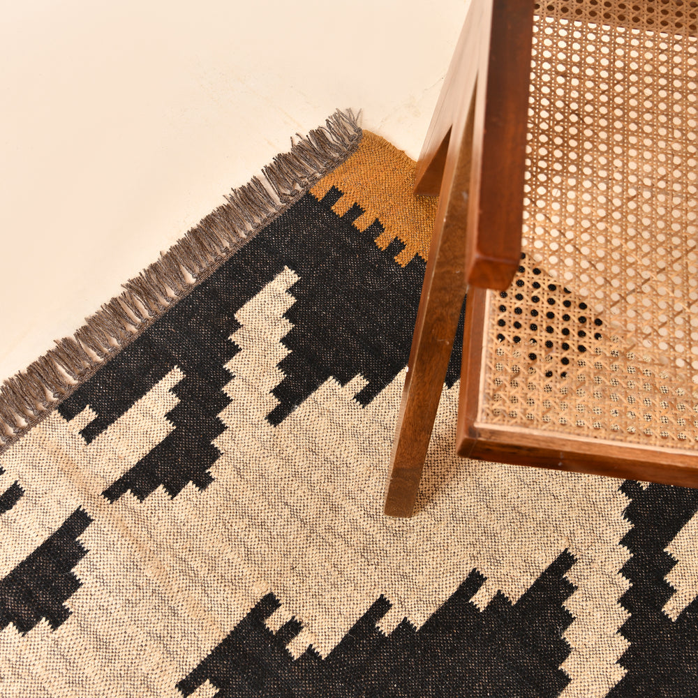 Handwoven ivory wool jute Kilim area rug featuring bold tribal geometric patterns with black, camel, and blush accents in a modern living room.