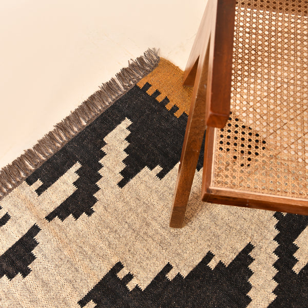 Handwoven ivory wool jute Kilim area rug featuring bold tribal geometric patterns with black, camel, and blush accents in a modern living room.