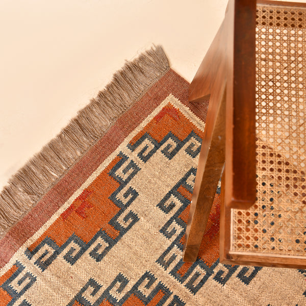 Handwoven wool jute kilim area rug with geometric tribal pattern in terracotta, ivory, and blue tones placed in a modern living room.