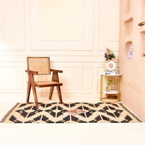 Handwoven black and ivory geometric kilim wool jute area rug in a modern living room with wooden chair and side table.