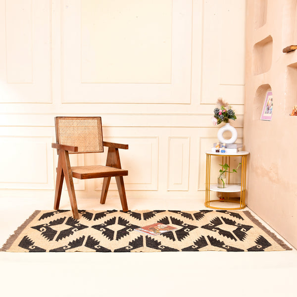 Handwoven black and ivory geometric kilim wool jute area rug in a modern living room with wooden chair and side table.