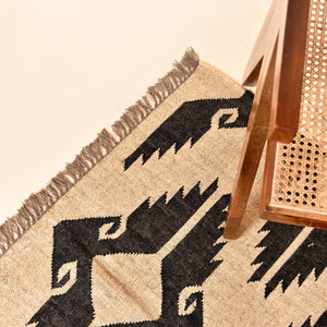 Handwoven black and ivory geometric kilim wool jute area rug in a modern living room with wooden chair and side table.