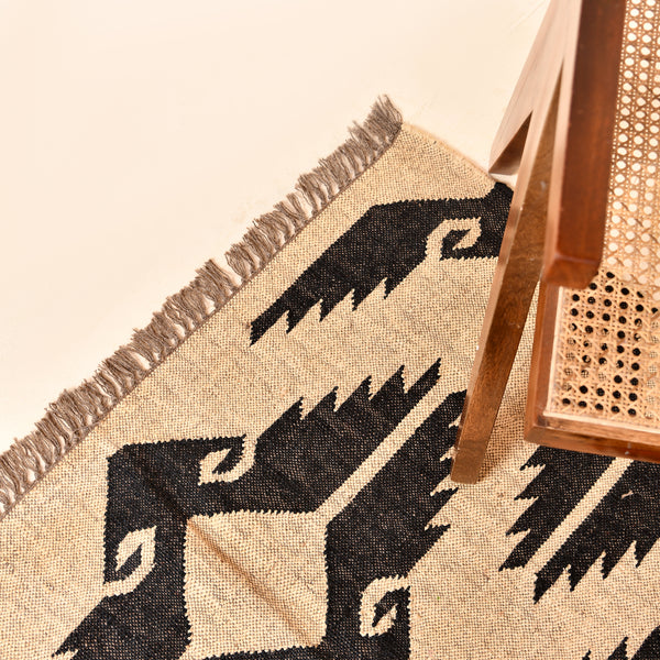 Handwoven black and ivory geometric kilim wool jute area rug in a modern living room with wooden chair and side table.