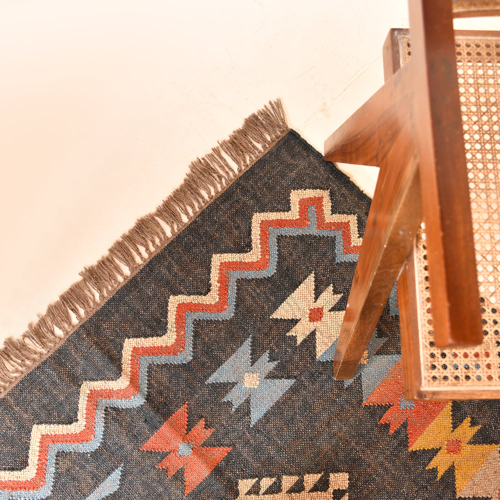Handwoven charcoal Kilim area rug with colorful Southwestern geometric tribal pattern and tassel edges displayed in a modern living room.
