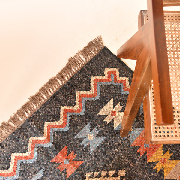Handwoven charcoal Kilim area rug with colorful Southwestern geometric tribal pattern and tassel edges displayed in a modern living room.
