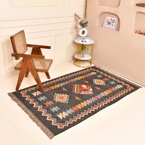 Handwoven charcoal Kilim area rug with colorful Southwestern geometric tribal pattern and tassel edges displayed in a modern living room.