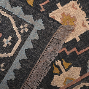 Handwoven black wool jute Kilim area rug with tribal geometric pattern and fringe in a modern living room.