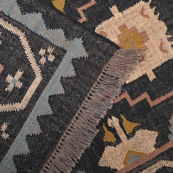 Handwoven black wool jute Kilim area rug with tribal geometric pattern and fringe in a modern living room.