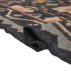 Handwoven black wool jute Kilim area rug with tribal geometric pattern and fringe in a modern living room.
