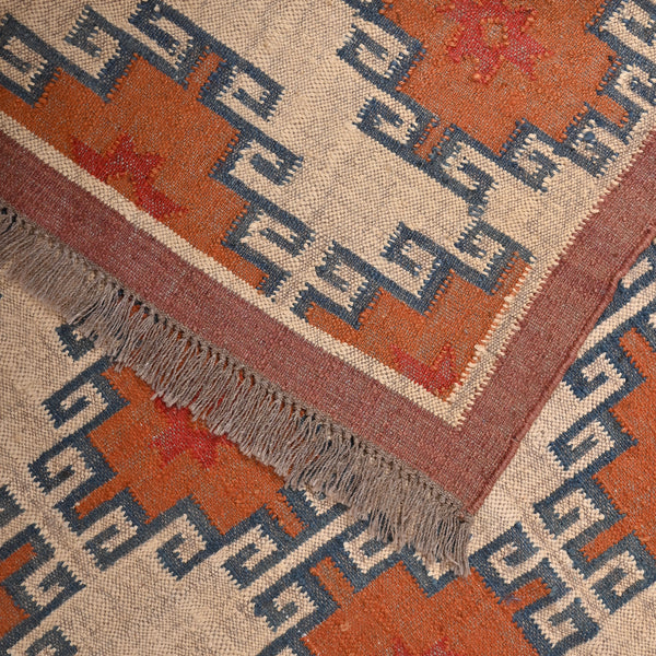 Handwoven wool jute kilim area rug with geometric tribal pattern in terracotta, ivory, and blue tones placed in a modern living room.