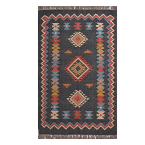 Handwoven charcoal Kilim area rug with colorful Southwestern geometric tribal pattern and tassel edges displayed in a modern living room.