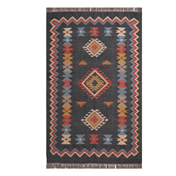 Handwoven charcoal Kilim area rug with colorful Southwestern geometric tribal pattern and tassel edges displayed in a modern living room.