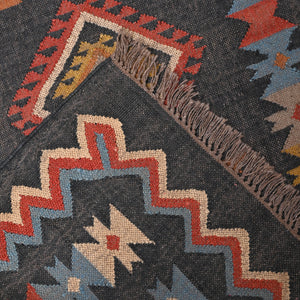Handwoven charcoal Kilim area rug with colorful Southwestern geometric tribal pattern and tassel edges displayed in a modern living room.