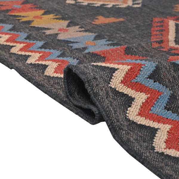 Handwoven charcoal Kilim area rug with colorful Southwestern geometric tribal pattern and tassel edges displayed in a modern living room.