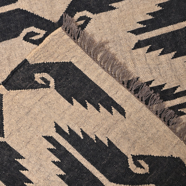 Handwoven black and ivory geometric kilim wool jute area rug in a modern living room with wooden chair and side table.