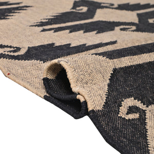 Handwoven black and ivory geometric kilim wool jute area rug in a modern living room with wooden chair and side table.