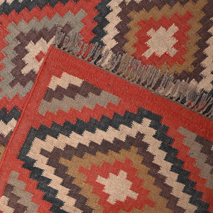 Handwoven geometric wool jute kilim area rug with tribal diamond pattern in terracotta, beige, charcoal, and ivory colors for living room and bedroom décor.