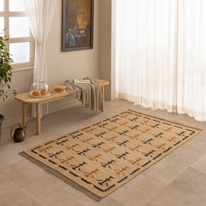 Handwoven mustard yellow and off-white geometric kilim jute rug with fringe trim, laid flat on a tile floor with a white ceramic vase and book lifestyle setting.