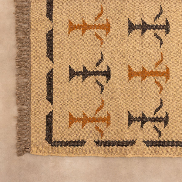 Handwoven mustard yellow and off-white geometric kilim jute rug with fringe trim, laid flat on a tile floor with a white ceramic vase and book lifestyle setting.