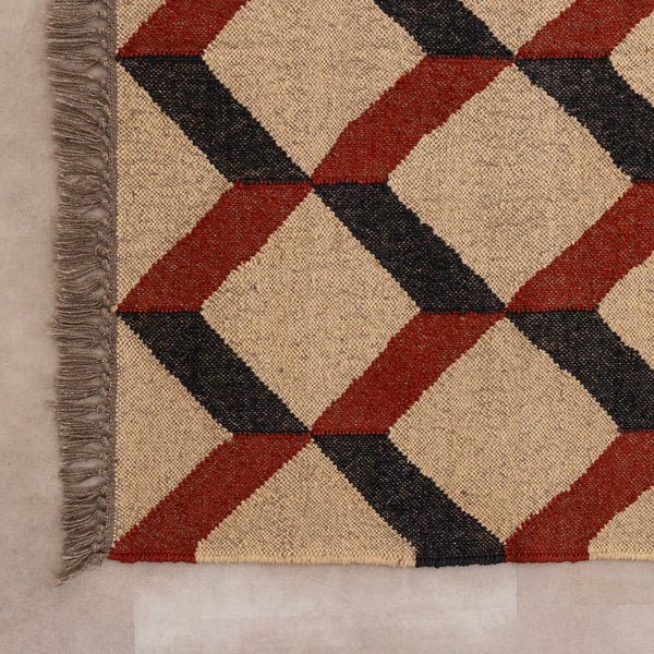 Handwoven jute and wool area rug featuring a 3D geometric optical cube pattern in terracotta rust, charcoal black, and natural beige, displayed on a tile floor with a ceramic vase and book.