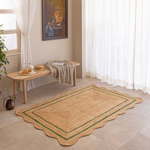 Handcrafted natural jute area rug with a double green border line and a wavy scalloped edge, displayed on a beige tile floor.