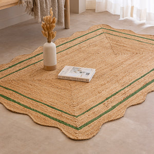 Handcrafted natural jute area rug with a double green border line and a wavy scalloped edge, displayed on a beige tile floor.
