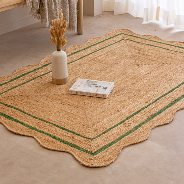 Handcrafted natural jute area rug with a double green border line and a wavy scalloped edge, displayed on a beige tile floor.