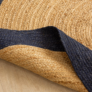 Natural beige circular jute rug with a dark navy border in a minimalist modern living room.