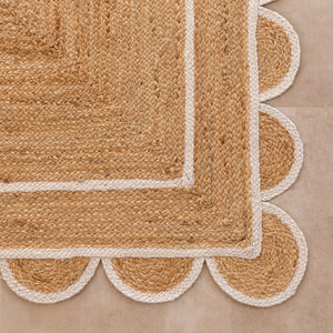 Handmade natural jute area rug with scalloped braided border in a neutral beige living room