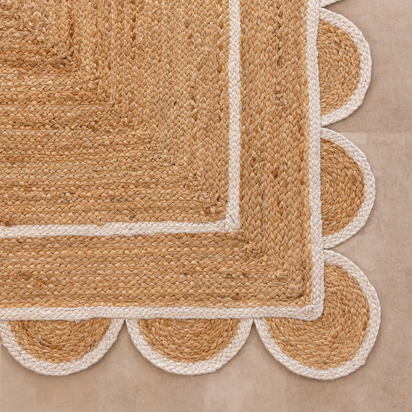 Handmade natural jute area rug with scalloped braided border in a neutral beige living room