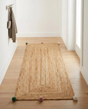 Handwoven natural jute runner rug with colorful pom-pom accents laid in a bright white hallway on light oak flooring