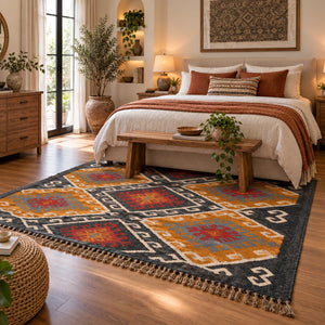Large handwoven Kilim wool rug with a traditional geometric diamond motif in ochre yellow, charcoal black, terracotta rust, and grey, displayed vertically on a metal rack.