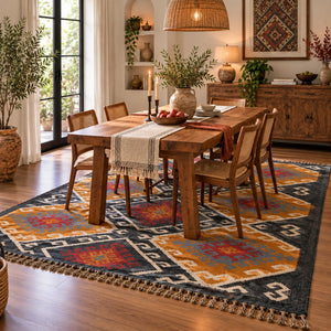 Large handwoven Kilim wool rug with a traditional geometric diamond motif in ochre yellow, charcoal black, terracotta rust, and grey, displayed vertically on a metal rack.